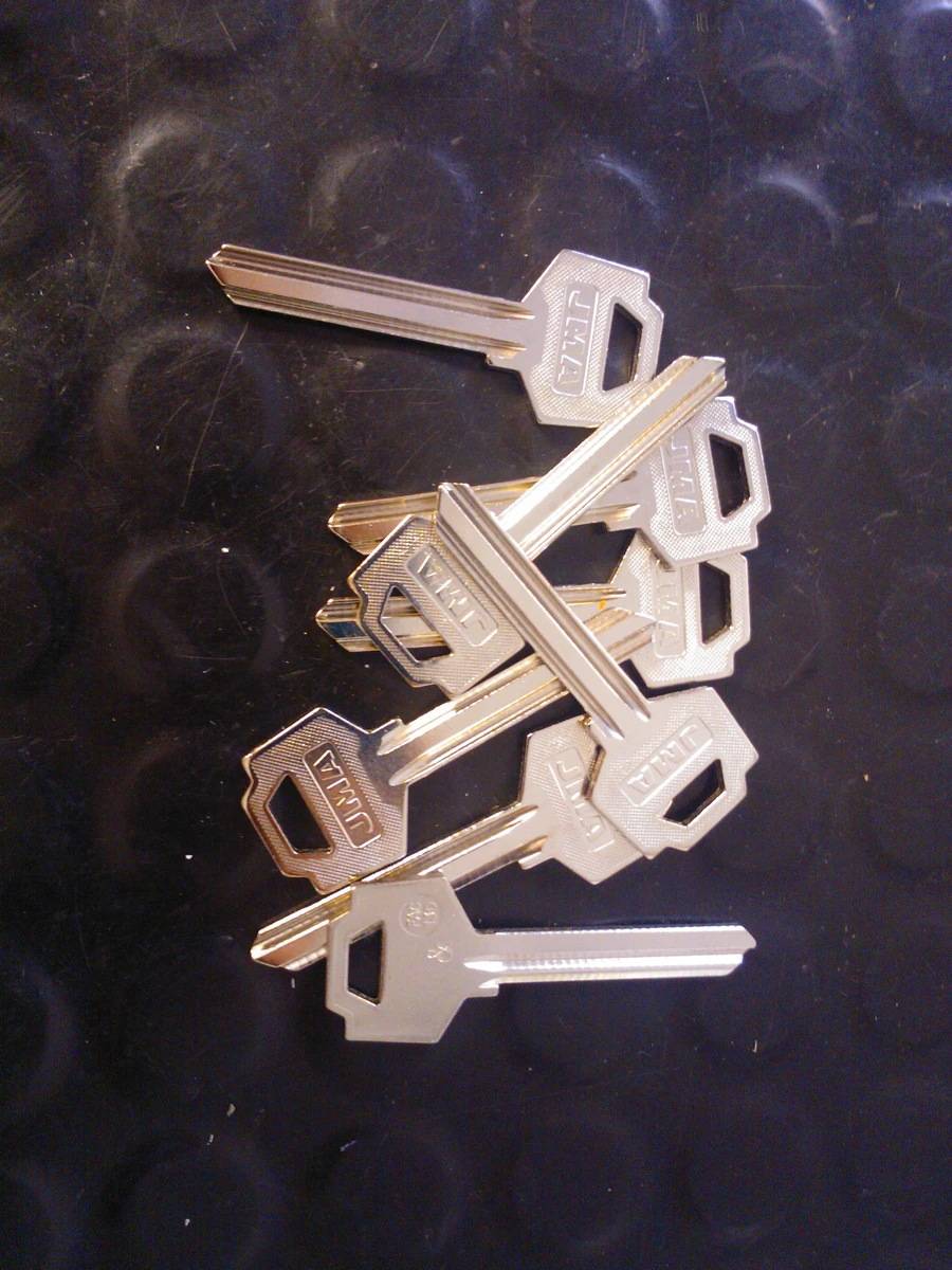 A pile of uncut brass key blanks with plain bows on a black rubber mat.