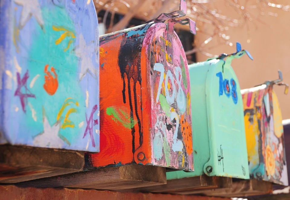 A row of hand painted rural curbside mailboxes with raised flags sitting on a wooden plank.